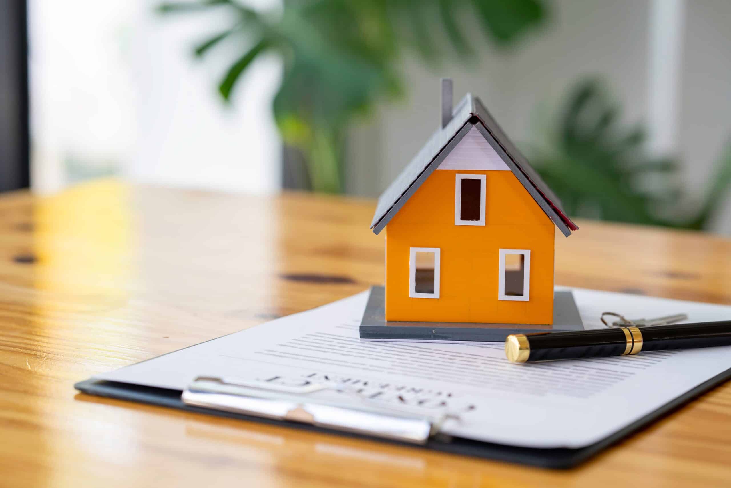 Model house on a clipboard with a signed document and pen
