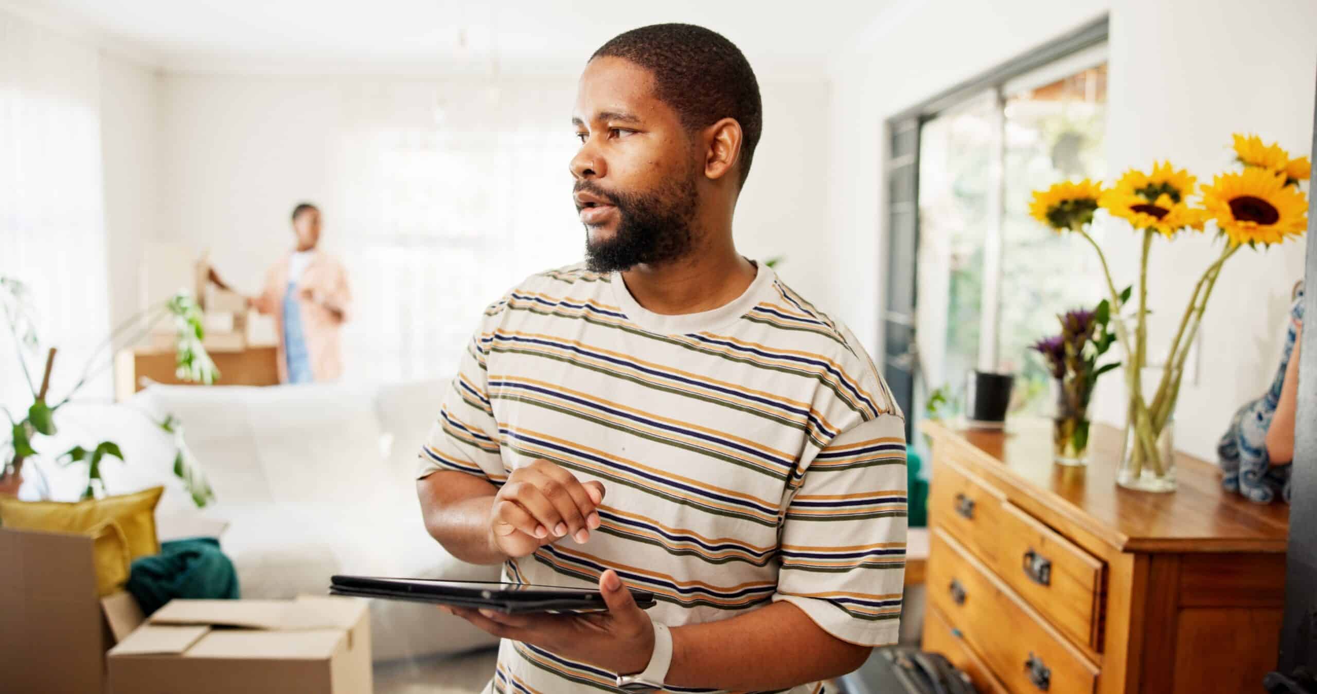 Man using a tablet in a living room while someone unpacks behind him