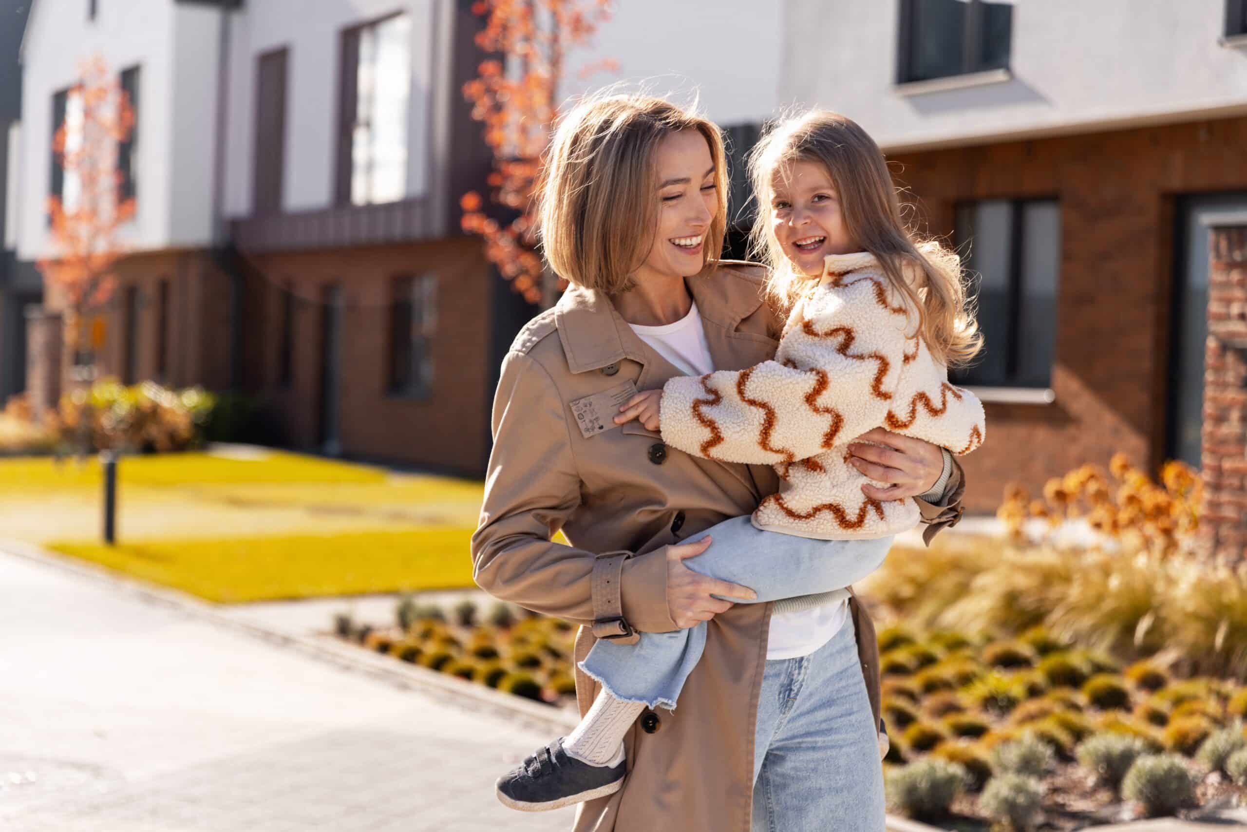 Woman carrying a young child outside a row of brick townhouses