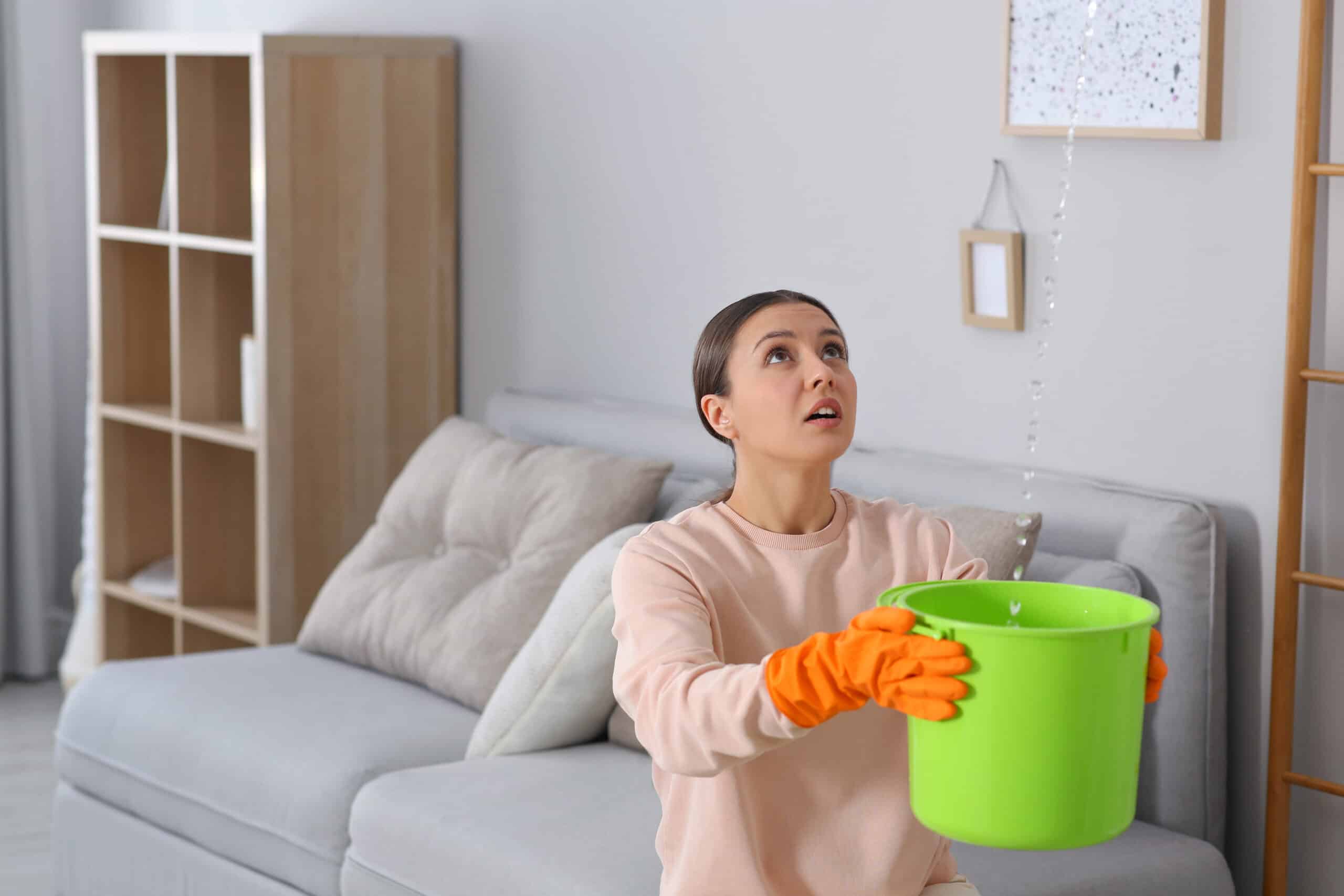 Woman holding a green bucket looking up at a ceiling leak