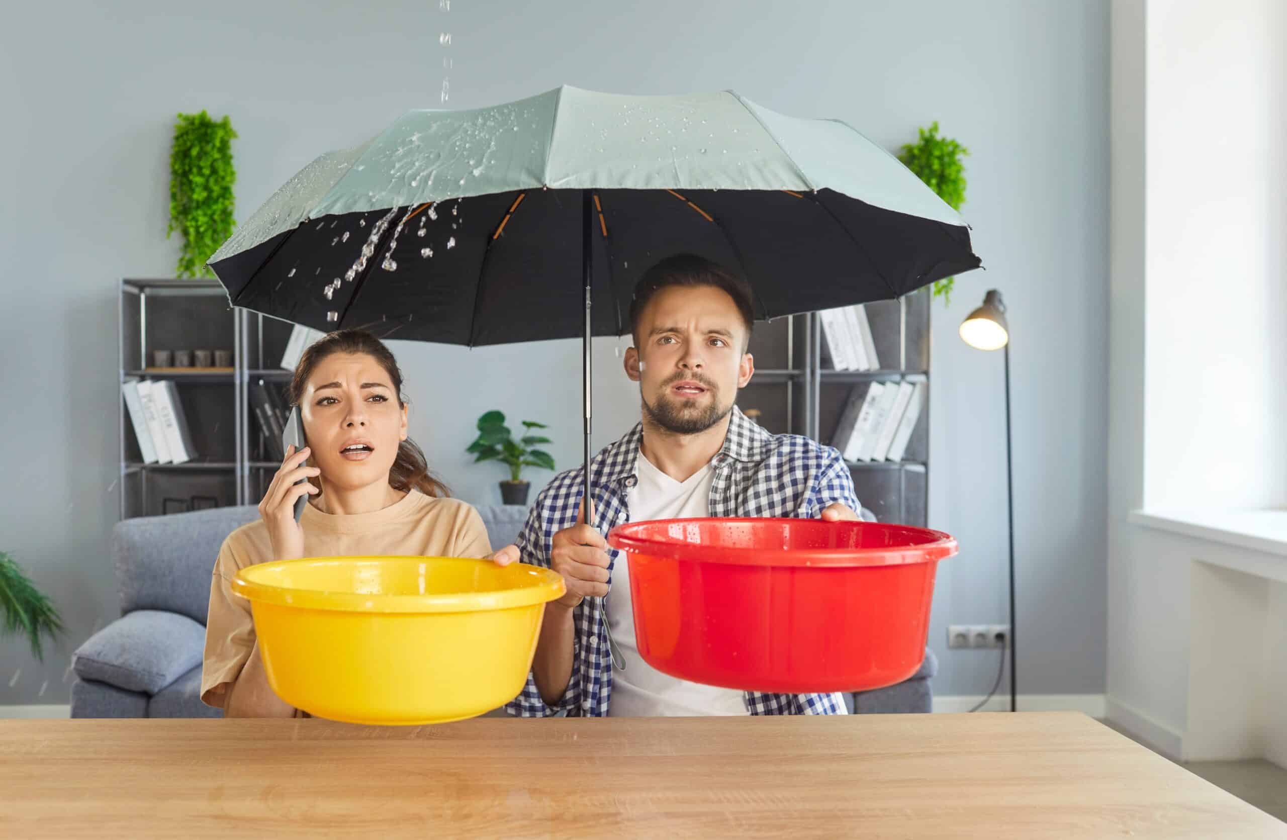 Couple sheltering under an umbrella indoors holding buckets