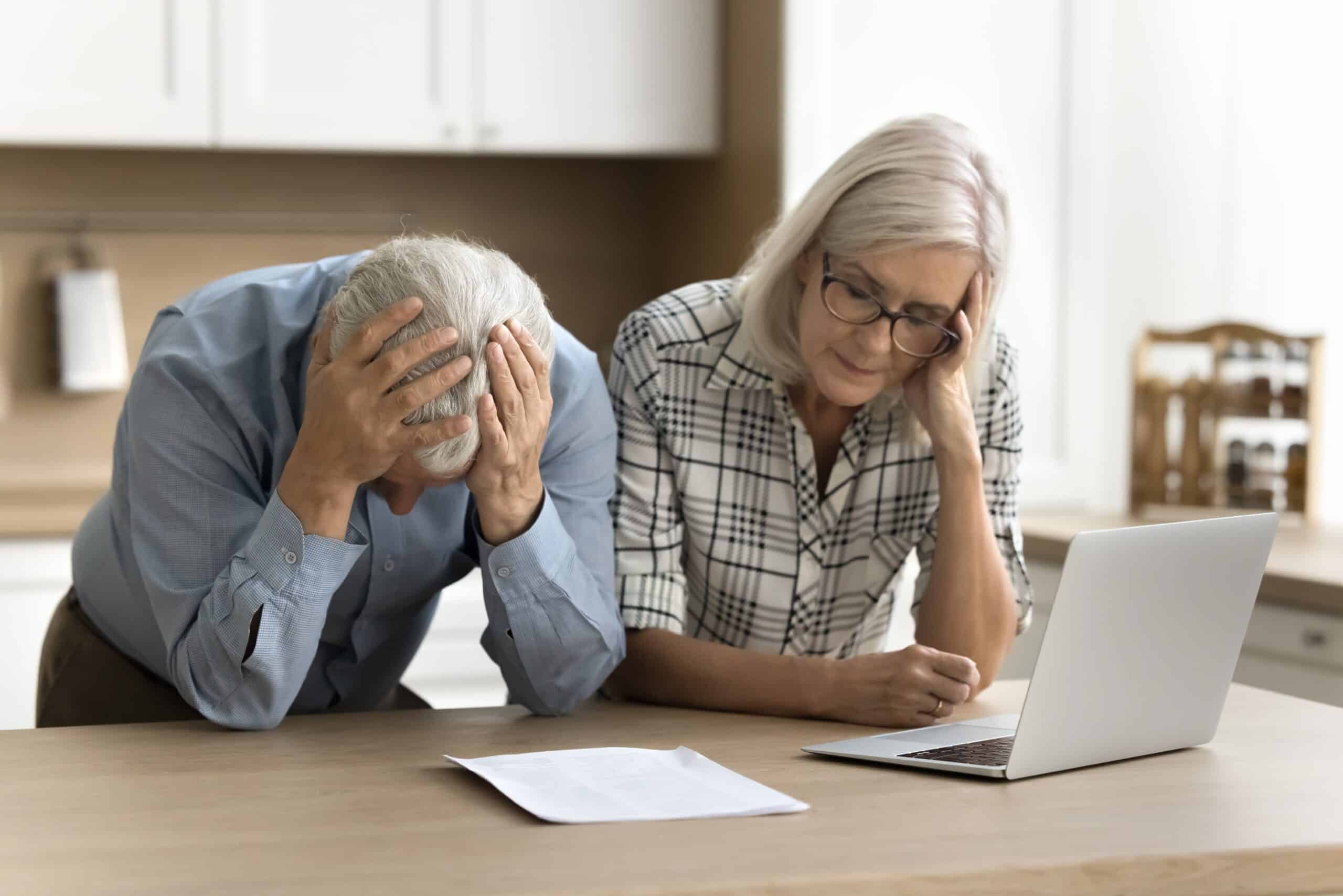 Older couple looking worried at a laptop and paperwork at a kitchen table