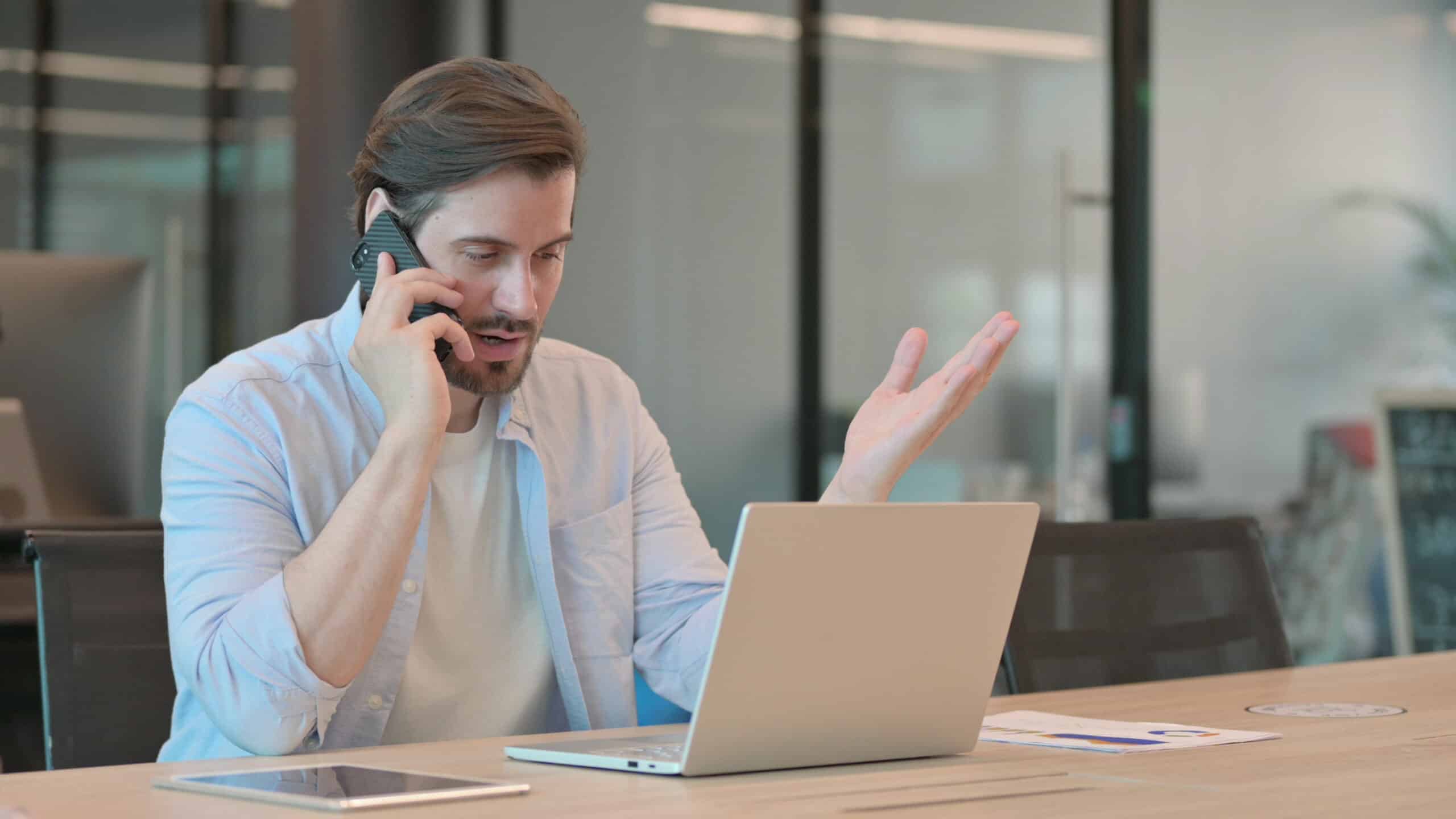 Frustrated man on the phone at a desk with a laptop