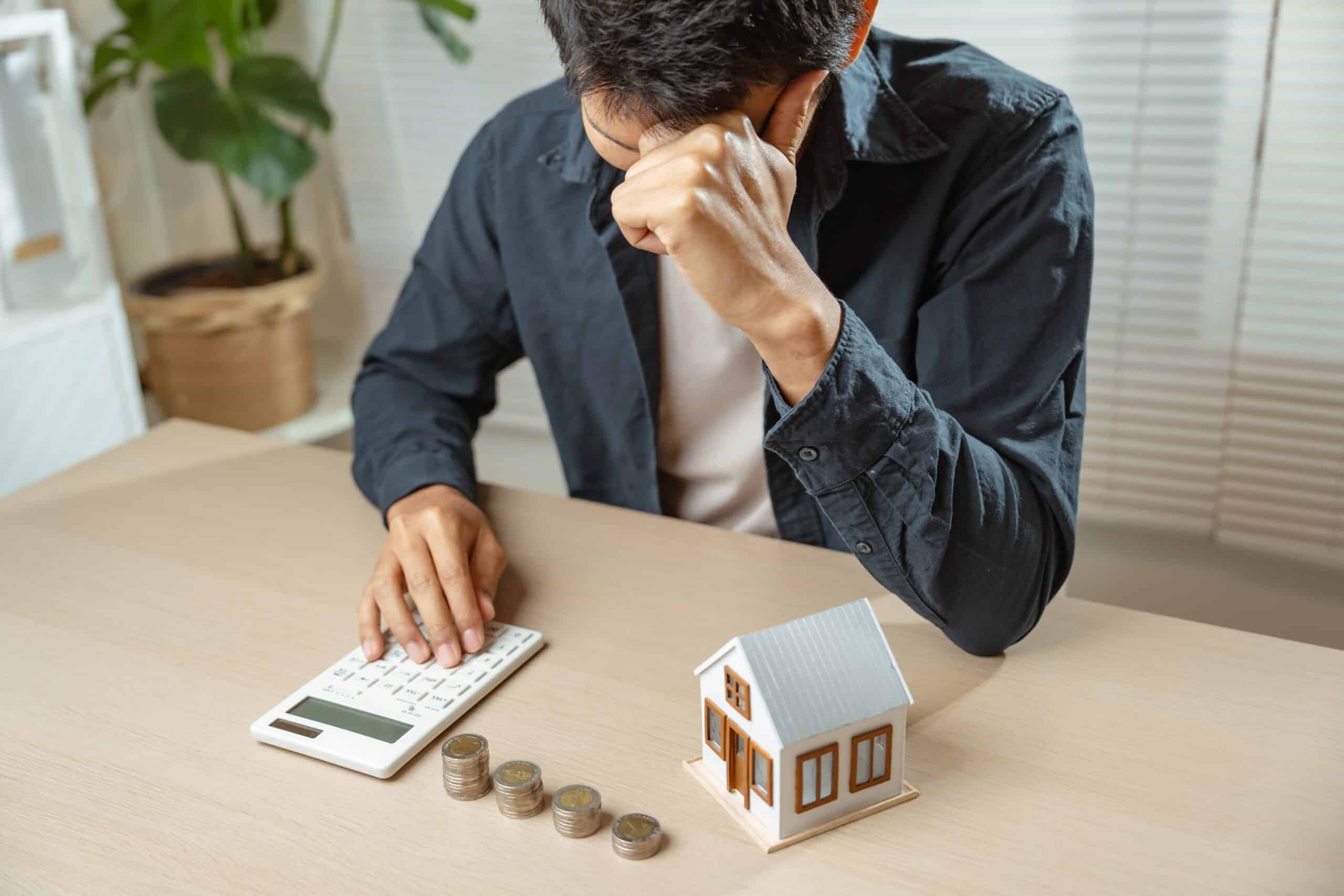 Man with his head in his hand at a calculator with coins and a model house