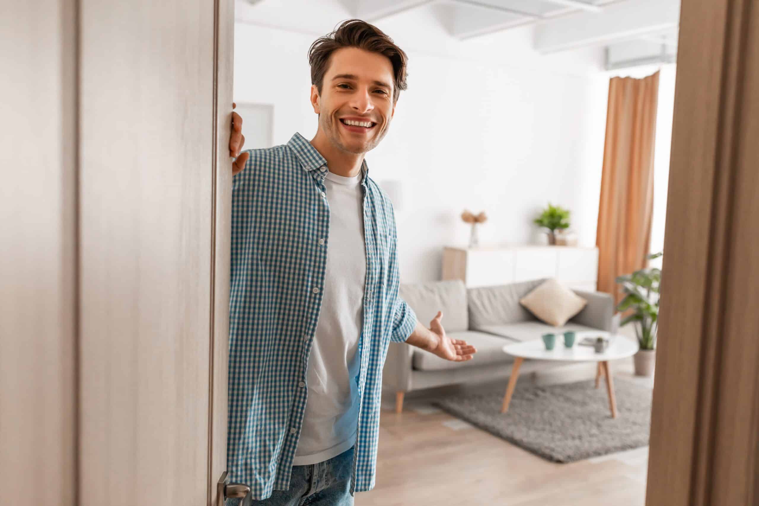 Smiling man opening the door into a bright furnished living room