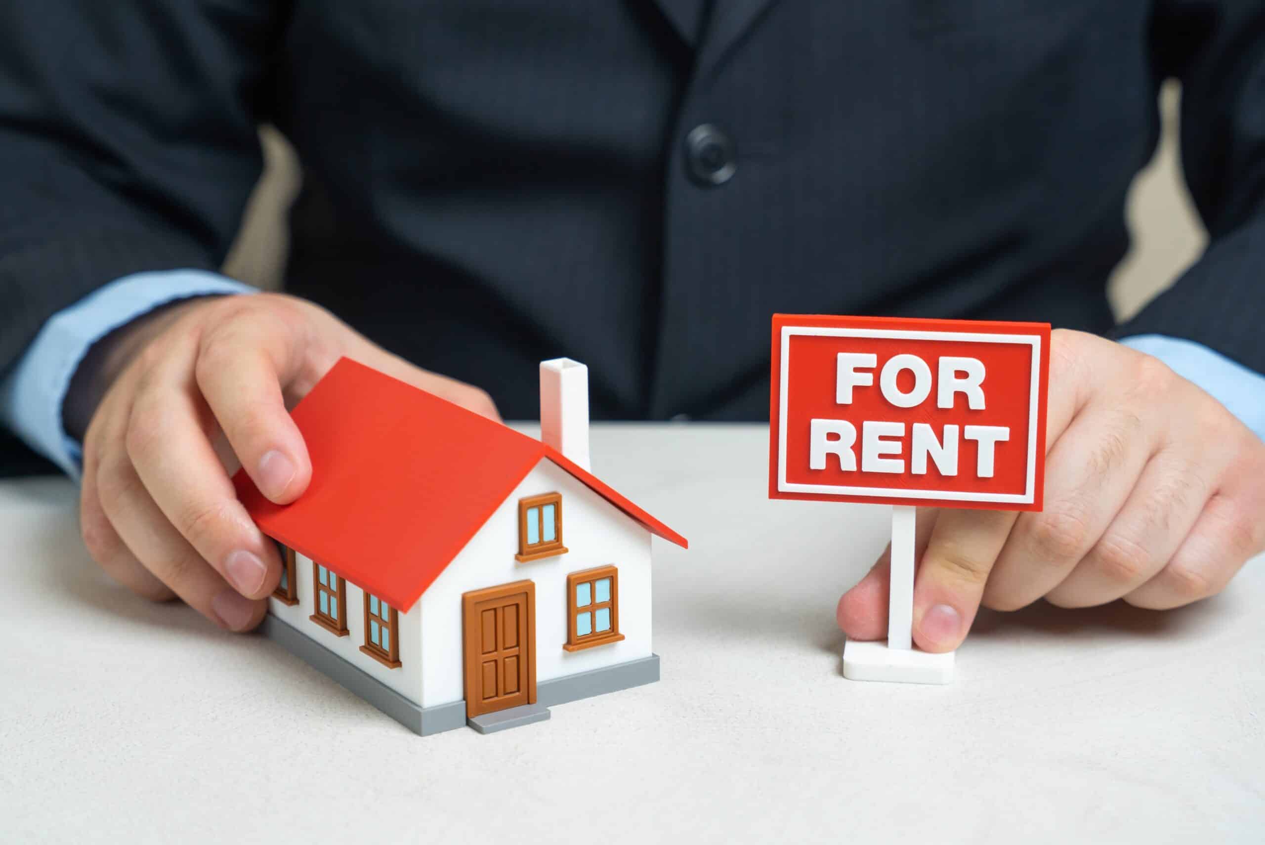 Hands placing a model house next to a red For Rent sign