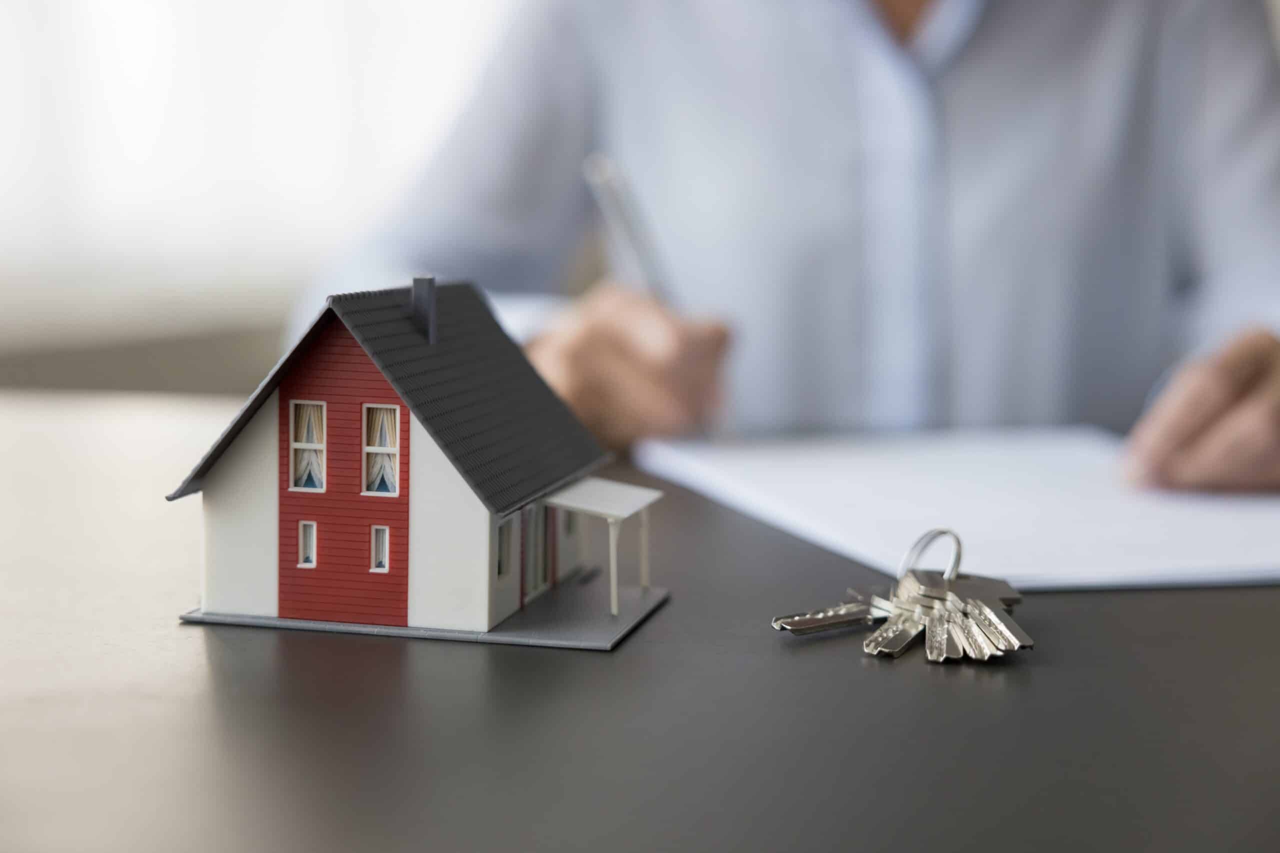 Person signing a document beside a model house and keys
