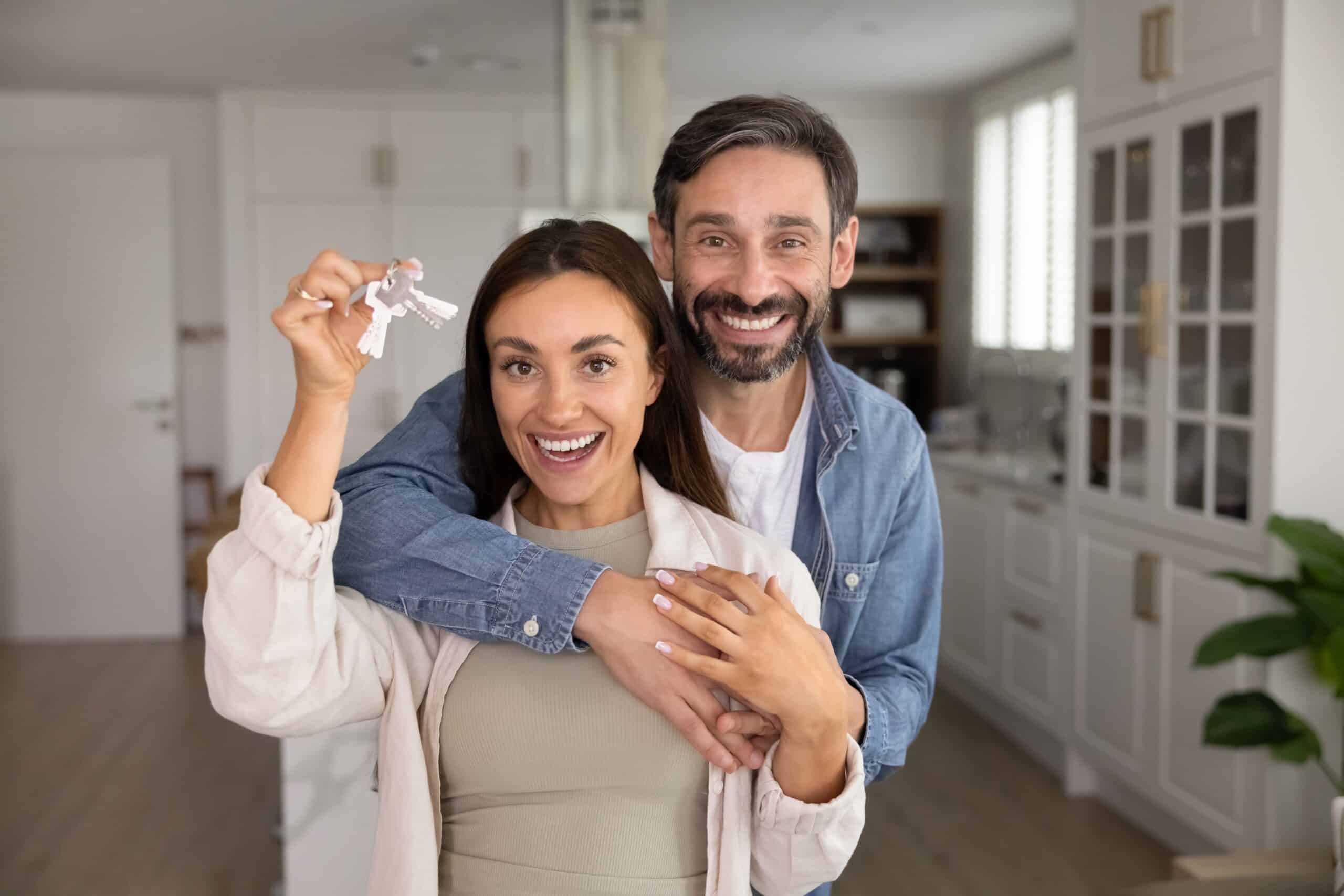 Smiling couple holding up keys in a new kitchen