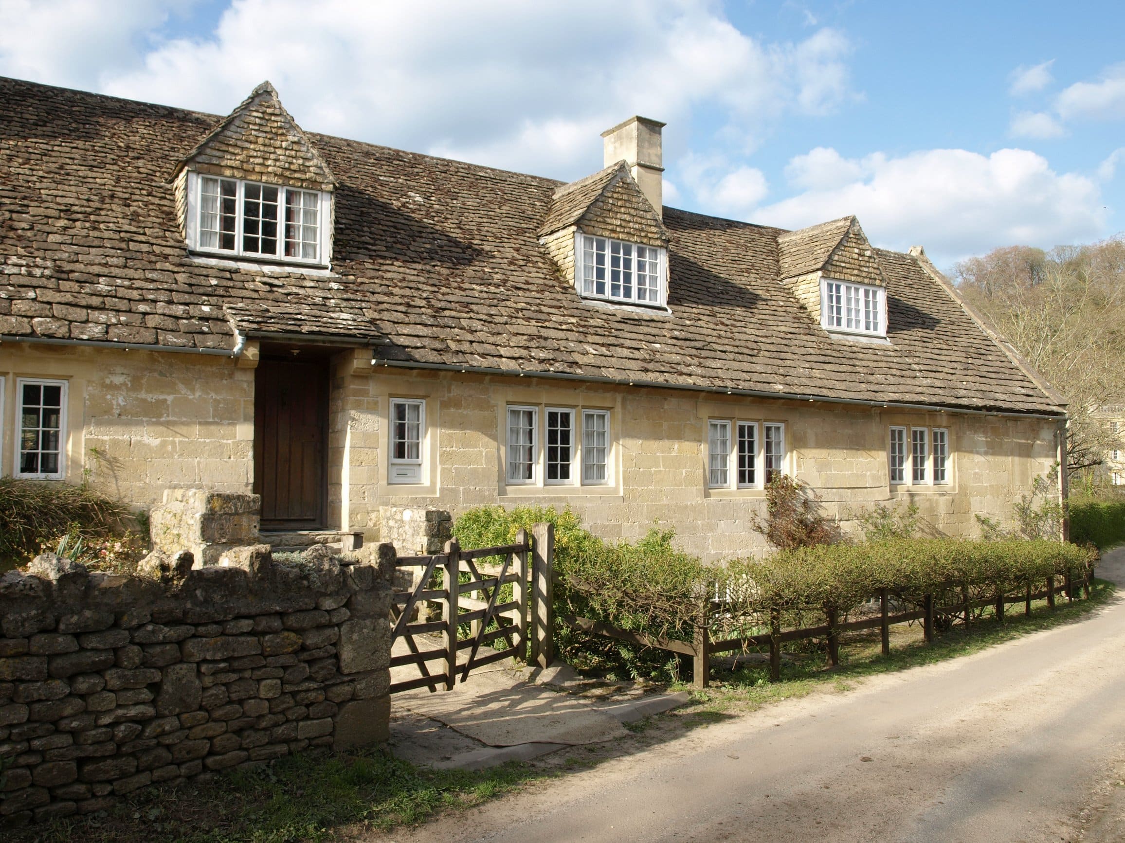 Large Cotswold stone house behind a wooden gate