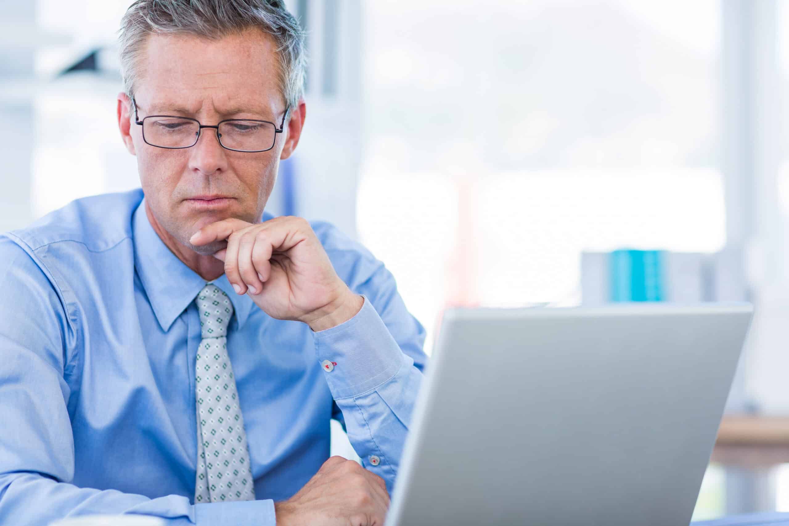 Man in a shirt and tie looking thoughtfully at a laptop