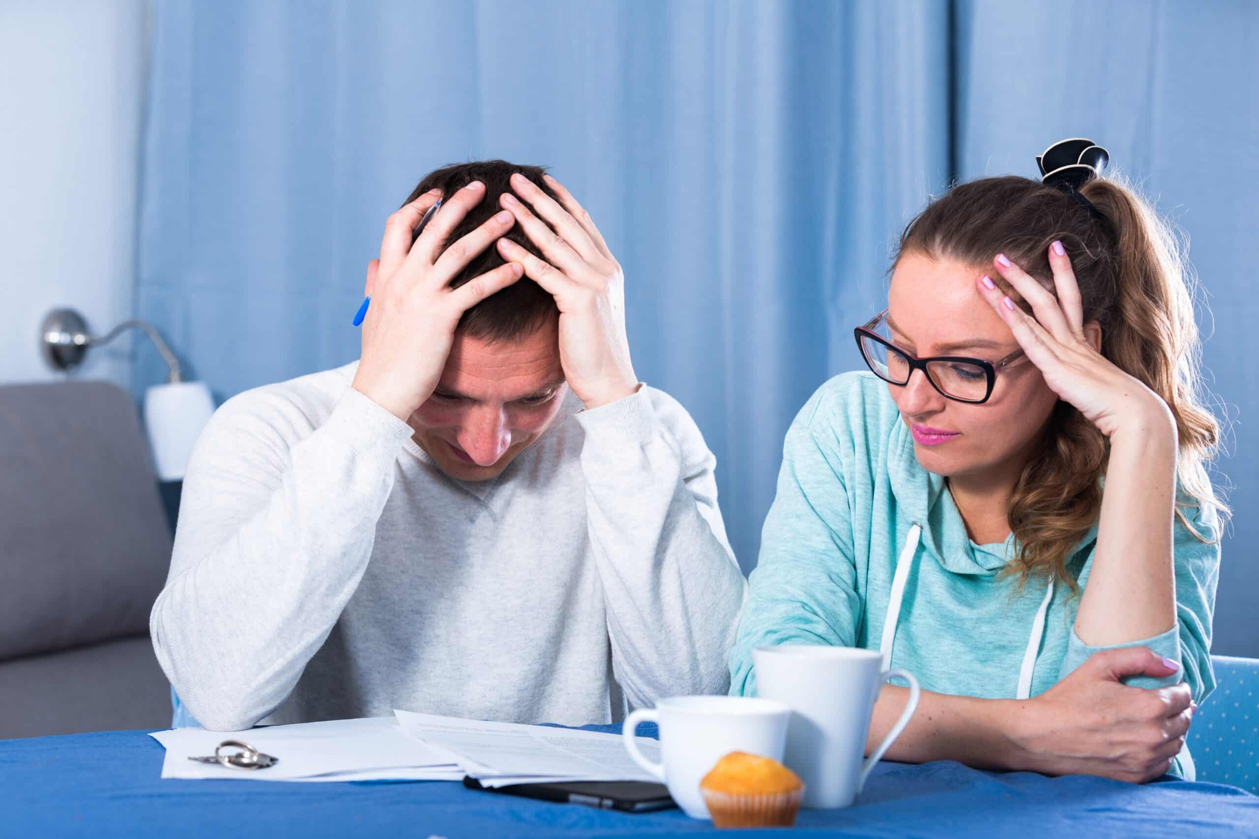 Stressed couple with their heads in their hands over paperwork