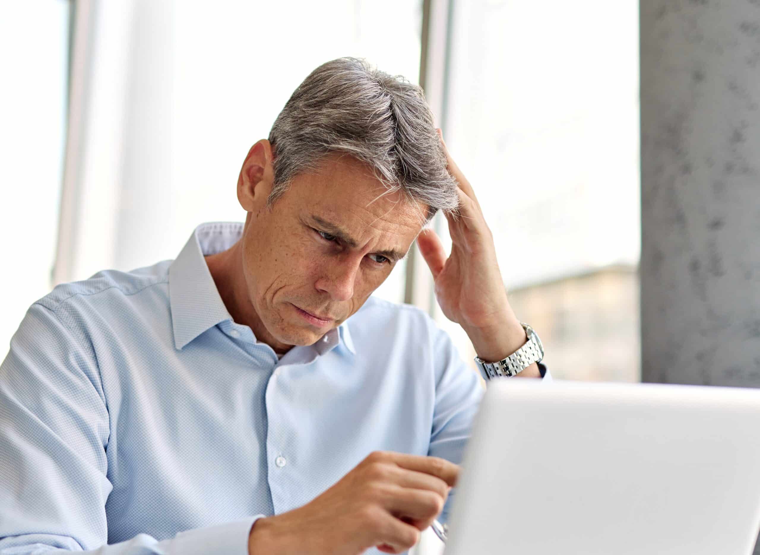 Worried man with his hand to his head at a laptop
